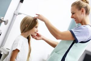 femme médecin mesurant la taille d'une fille à la clinique photo