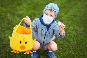 petit garçon portant un masque de protection à la recherche d'oeufs de pâques dans le jardin de printemps. photo