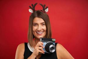 femme heureuse adulte dans l'ambiance de noël prenant des photos instantanées sur fond rouge