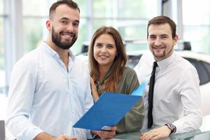 jeune vendeur confiant expliquant les caractéristiques de la voiture aux jeunes propriétaires attrayants photo