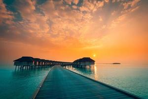 coucher de soleil sur l'île des maldives. complexe de bungalows sur pilotis à la plage des îles. océan indien, maldives. beau paysage de coucher de soleil, complexe de luxe et ciel coloré. coucher de soleil artistique sur la plage sous un ciel magnifique photo