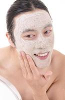 procédure de beauté et soins de la peau. portrait en gros plan d'un homme asiatique aux seins nus heureux qui rit avec un masque facial touchant son visage. isolé sur fond blanc. photo