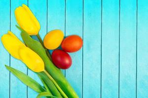 tulipes jaunes avec des oeufs de couleur rouge, orange et jaune sur fond turquoise. fond de Pâques. copie espace photo