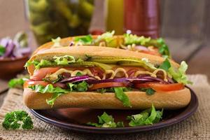 Hot-dog avec cornichons, tomates et laitue sur fond de bois photo