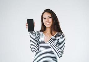 jeune femme asiatique heureuse aux cheveux longs en manches longues rayées utilisant un téléphone portable sur la maquette de fond blanc photo