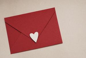 gros plan d'une enveloppe en papier rouge avec un coeur blanc sur fond marron neutre. concept d'amour et de saint valentin. photo
