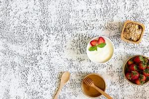 vue de dessus du yaourt aux fraises dans un bol en bois avec granola, miel, menthe et fraise fraîche sur fond de bois. concept d'aliments santé. photo