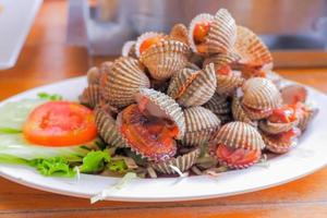 les coques cuites à la vapeur les coques bouillies sont placées sur une assiette blanche. garni de tranches de tomates. photo