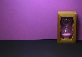 sablier de sable rose en bois. petite décoration photo en verre de sable isolée sur fond violet et noir. pas de texte avec un espace pour l'espace de copie.