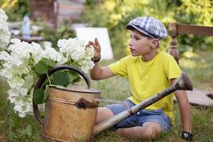 l'enfant travaille dans le jardin. garçon avec un arrosoir vintage et un bouquet de fleurs. photo