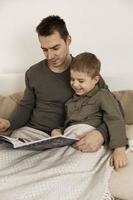 père et fils lisant un livre sur le lit à la maison. jeune homme séduisant et petit garçon se reposant dans la chambre. couleurs naturelles de la terre. environnement cosy. père lit un conte de fées pour son enfant. photo