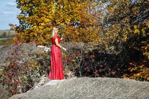 fille en robe rouge sur roche ou béton structure en ruine avec rowan sur fond d'automne photo