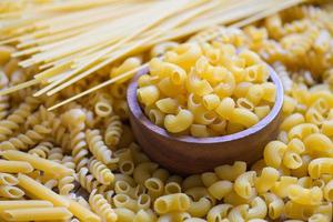 macaronis crus sur bol en bois, pâtes diverses sortes de pâtes non cuites spaghettis et nouilles sur fond, concept culinaire de cuisine italienne, collection de différentes pâtes crues pour la cuisson des aliments photo