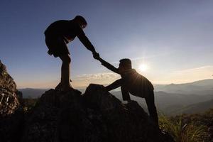 silhouette de coup de main entre deux grimpeur. couple randonnée s'entraident silhouette dans les montagnes avec la lumière du soleil. les hommes aidant à tirer les gens des hautes falaises photo