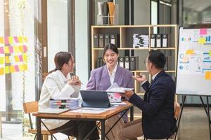 L'équipe commerciale asiatique se compose de personnel de marketing. le comptable et le responsable financier s'entraident pour analyser les bénéfices de l'entreprise à l'aide de tablettes. calculatrices, ordinateurs portables, papier millimétré et stylos d'entreprise. photo