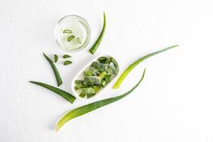 gel d'aloe vera universel dans un pot cosmétique en verre et tranches d'aloe juteuses dans un bol ovale en céramique. vue de dessus. fond blanc. photo