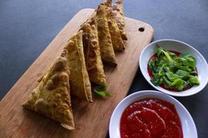 samosa, samsa ou somsa sont des pâtisseries frites triangulaires ou des pastri servis avec de la sauce tomate et une tranche de poireau, sur fond noir photo