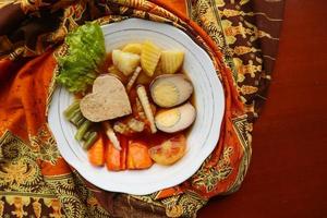 selat solo est une salade traditionnelle d'indonésie. à base d'œufs durs, de pois chiches bouillis, de carottes bouillies, de pommes de terre rissolées et de laitue, de steak ou de bistik. servi sur table en bois photo