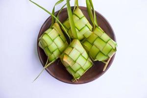 ketupat dans une assiette en terre cuite isolée sur fond blanc. La boulette de riz ketupat est un aliment servi lors de l'idhul fitri eid mubarak en indonésie, à base de riz enveloppé dans de jeunes feuilles de coco janur photo