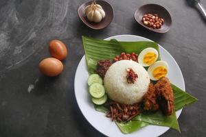 nasi lemak, est des œufs durs traditionnels malais, des haricots, des anchois, de la sauce chili, du concombre. du plat servi sur une feuille de bananier photo