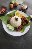 nasi lemak, est des œufs durs traditionnels malais, des haricots, des anchois, de la sauce chili, du concombre. du plat servi sur une feuille de bananier photo