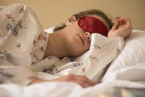 femme fatiguée dormant dans son lit portant un masque de sommeil avec les yeux bandés photo