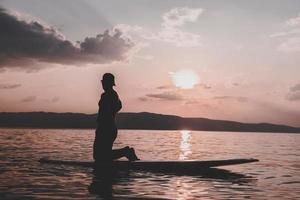 jeune homme sportif sur sup paddle board allant à la mer au coucher du soleil. photo