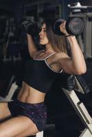 bodybuilder femme avec un corps bronzé faisant de l'exercice dans la salle de gym soulever des poids photo