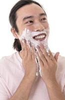 portrait en gros plan d'un homme asiatique avec de la mousse à raser sur son visage, rasant sa barbe avec un rasoir. isolé sur fond blanc photo