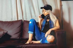 glamour jeune femme blonde est assise sur un canapé dans des vêtements décontractés et des écouteurs sur le cou photo