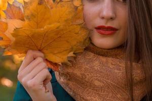 fille avec rouge à lèvres garde les feuilles d'érable orange à la main, gros plan photo