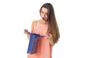 Jeune fille surprise à la recherche dans un sac cadeau bleu isolé sur fond blanc photo