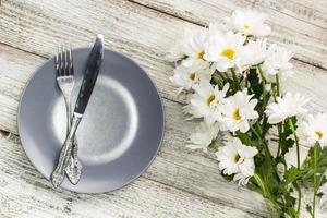 assiette vide avec fourchette et couteau décoré de fleurs de camomille sur fond de bois blanc photo
