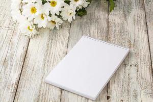 bouquet de printemps de marguerites blanches avec cahier propre pour écrire sur une table en bois blanc photo