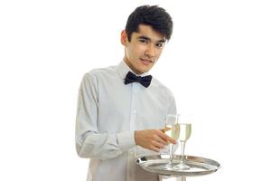 charmant jeune serveur sourit, regarde la caméra et tient un plateau avec des verres de champagne photo