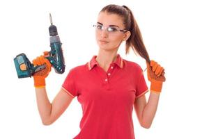 jeune jolie femme brune constructeur en uniforme avec des lunettes et une perceuse dans ses mains faire des rénovations isolées sur fond blanc photo