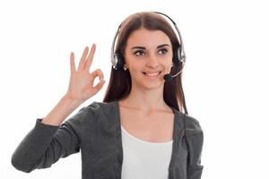 Jeune femme d'affaires brune mignonne avec un casque et un microphone souriant et et montrant ok isolé sur fond blanc photo