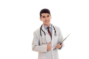 jeune beau médecin en uniforme bleu avec stéthoscope sur son cou prendre des notes et des sourires isolés sur fond blanc photo