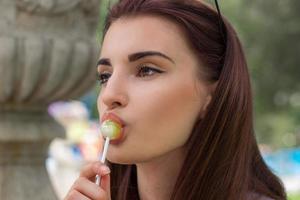 portrait en gros plan d'une belle fille brune lèche une sucette photo