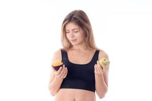 fille athlétique en haut noir tient un petit gâteau et pomme à la main isolé sur fond blanc photo