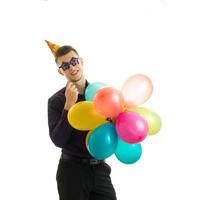 merveilleux jeune homme avec un cône sur la tête garde près du visage des verres en papier des ballons et souriant photo