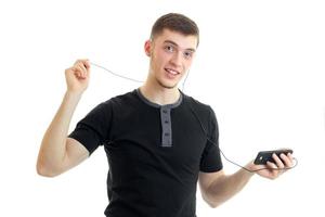 joyeux jeune homme dans un t-shirt noir tient des écouteurs avec le téléphone photo