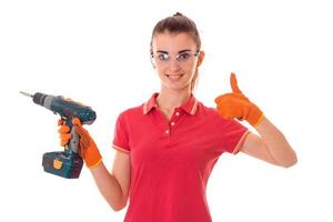 souriante jeune fille brune constructeur en uniforme et lunettes fait la rénovation et montrant les pouces vers le haut isolé sur fond blanc photo