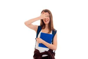 fille gaie avec un sac à dos sur le dos tenant un dossier et ferme les yeux avec l'autre main isolé sur fond blanc photo