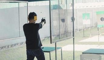 tireur asiatique homme portant un casque antibruit et des vêtements noirs pratiquant le tir à l'arme courte sur le champ de tir. sports de tir pour la méditation et l'autodéfense, activités récréatives. photo