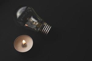 lampe électrique et bougie sur fond sombre. symbole du retour vers le passé. ampoule à incandescence et bougie. coupure de courant ou coupure de courant. prix élevés de l'électricité. économie d'électricité. photo