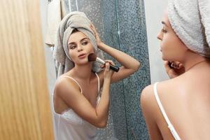 femme avec une serviette sur la tête, se regardant dans le miroir et se maquillant photo