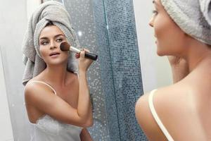 femme avec une serviette sur la tête, se regardant dans le miroir et se maquillant photo
