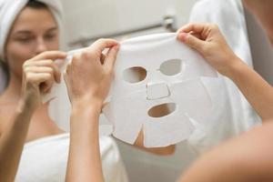 femme dans la salle de bain applique un masque facial en feuille photo