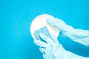 concept de vaisselle, mains dans des gants en caoutchouc pour tenir une éponge bleu clair et laver la vaisselle